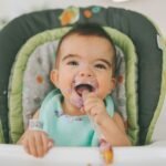 A messy baby eating blueberry yogurt in his high chair