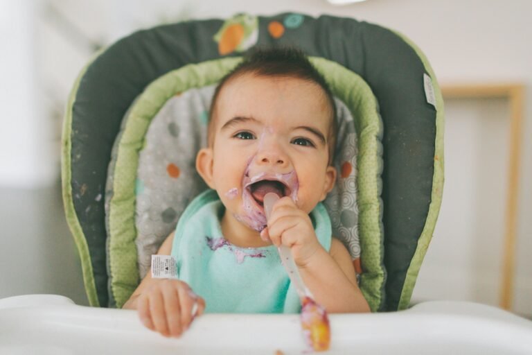 A messy baby eating blueberry yogurt in his high chair