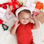 Adorable baby in Santa hat napping with Xmas gifts