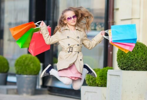 Adorable little girl walking with shopping bags outdoors in Europe. Fashion toddler kid in european