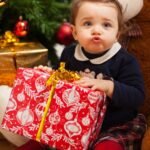 Toddler girl with gifts near christmas tree.