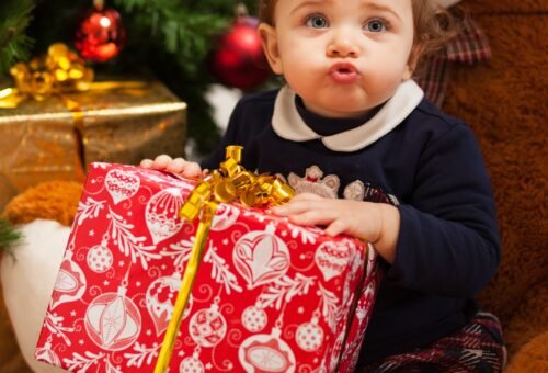 Toddler girl with gifts near christmas tree.