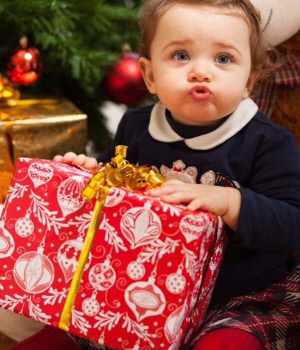 Toddler girl with gifts near christmas tree.