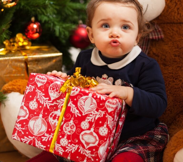 Toddler girl with gifts near christmas tree.