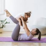 Young woman fit mom with baby girl doing fitness on mat at home