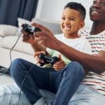 Playing video games. African american father with his young son at home